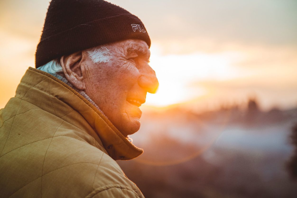 an elderly man closeup against a sunset