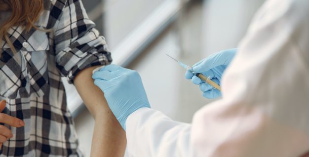 Closeup of a nurse in gloves giving a woman in a plaid shirt a vaccine, highlighting employee vaccine mandates