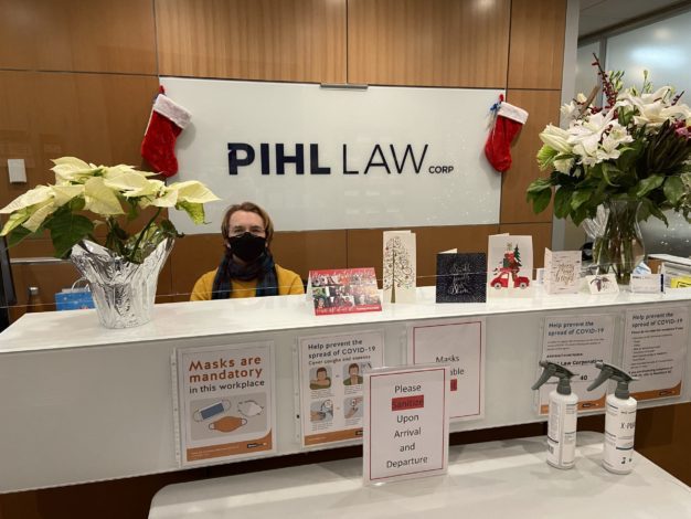 Pihl law office reception desk with receptionist, happy holidays cards, poinsettias, hanging stockings, and a covid sanitation station