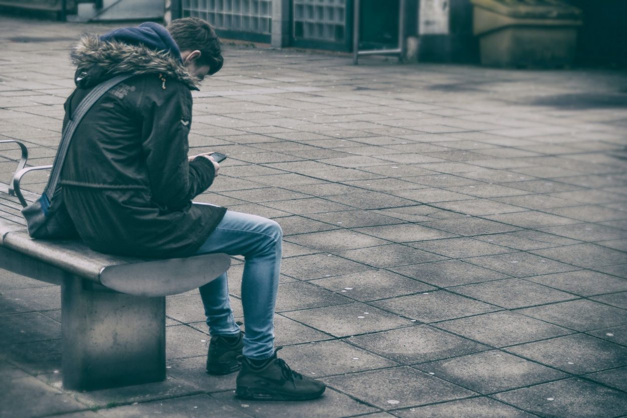 a worker sitting on a bench on a gray day looking down at his phone